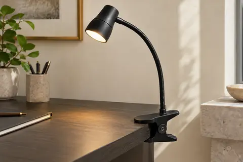 Lampe de bureau noire à pince et col flexible, fixée à un bureau en bois et allumée.