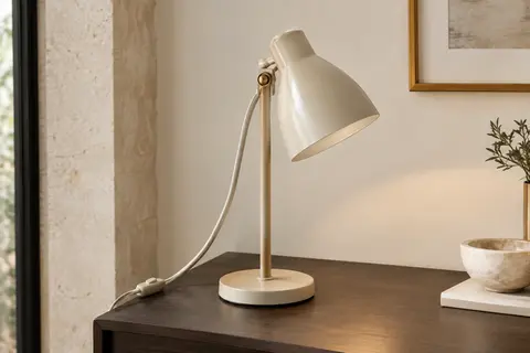 Lampe de chevet en métal beige à tête orientable, posée sur une table en bois fumé près d’un mur ivoire.