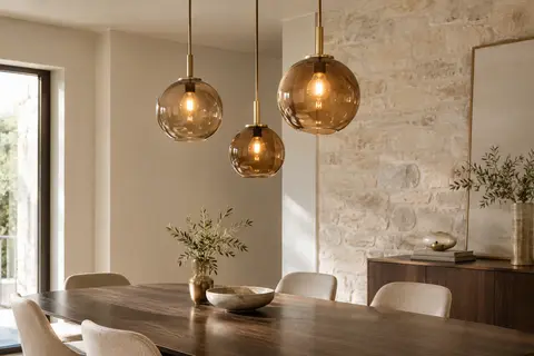 Suspension de plafond à trois globes en verre ambré installée au-dessus d’une table en bois.