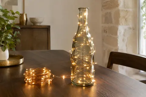 Guirlande LED blanc chaud à fil de cuivre enroulée autour d’une bouteille en verre