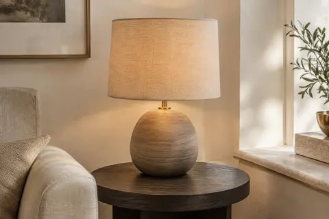 Lampe de table avec socle en béton effet bois et abat-jour en lin sable sur une table d’appoint.