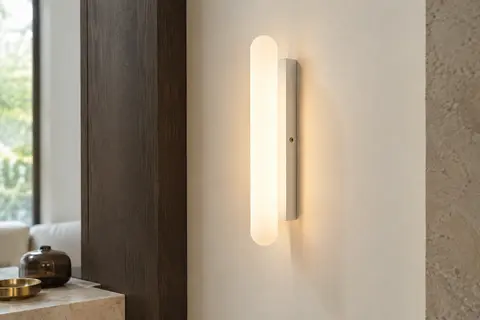 Applique murale Goeco blanche à diffuseur acrylique, allumée sur un mur ivoire dans un intérieur sobre.
