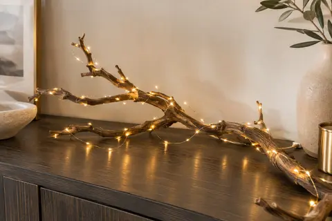 Guirlande de 120 micro LED blanc chaud disposée en courbes autour d’une branche sur une console claire.