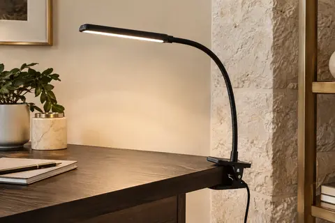 Lampe de bureau noire à pince et bras flexible, fixée au bord d’un bureau en bois