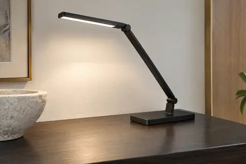 Lampe de bureau LED noire à tête inclinable et bras articulé, posée sur un bureau en bois.
