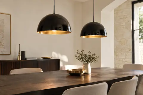 Deux suspensions en métal à dôme et intérieur doré au-dessus d’une table dans un intérieur sobre.