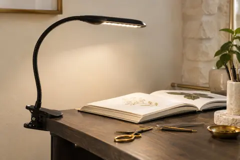 Lampe de bureau noire à pince, avec col de cygne flexible et tête LED allongée fixée à un bureau.