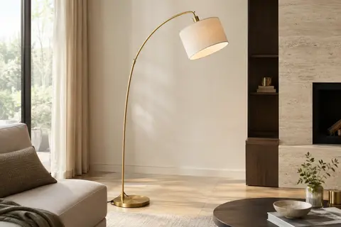 Lampadaire arc doré avec abat-jour beige, installé près d’un fauteuil dans un salon lumineux