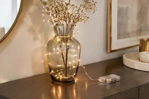 Guirlande LED blanc chaud sur fil cuivre flexible, disposée autour d’un vase en verre