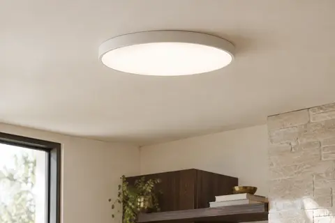 Plafonnier LED rond et plat Ouila diffusant une lumière blanc neutre dans un intérieur aux tons clairs.
