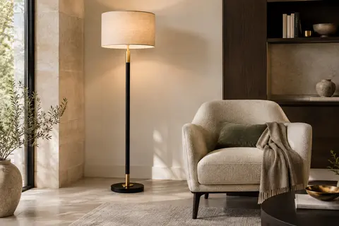 Lampadaire à structure noire et dorée avec abat-jour en lin diffusant une lumière douce près d’un fauteuil