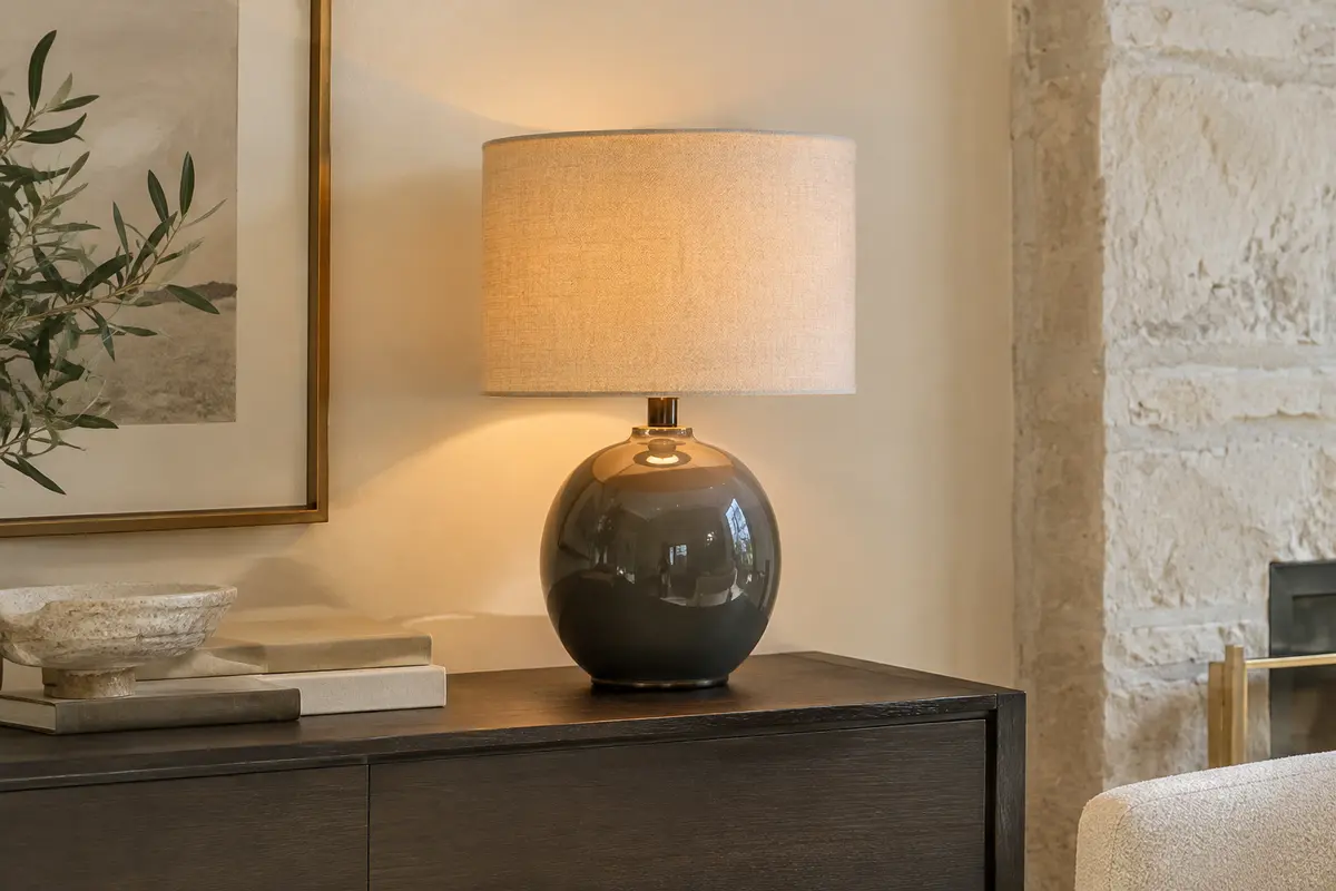 Lampe à poser Pauleen avec pied rond en céramique brillante et abat-jour en tissu beige, sur une console