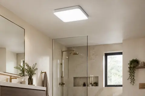 Plafonnier LED carré blanc et plat allumé au plafond d’une salle de bains aux tons ivoire et pierre claire