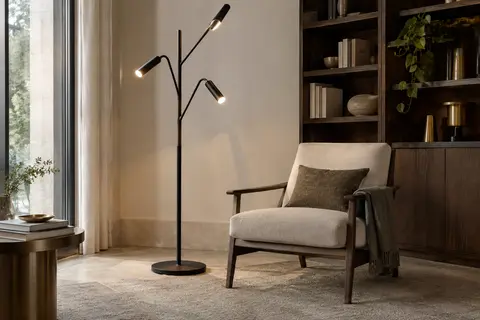 Lampadaire noir à trois têtes orientables près d’un fauteuil, diffusant une lumière douce dans un salon.