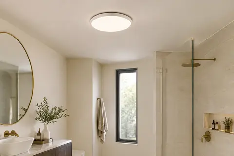 Plafonnier LED rond blanc et fin installé au plafond d’une salle de bain claire.