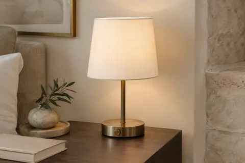 Lampe de table Visdanfo à pied bronze et abat-jour blanc en tissu, allumée sur une table de chevet