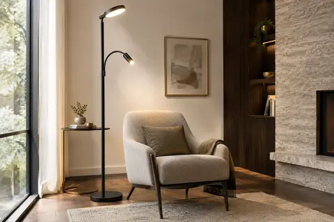 Lampadaire LED noir à deux têtes orientables installé près d’un fauteuil dans un salon lumineux.